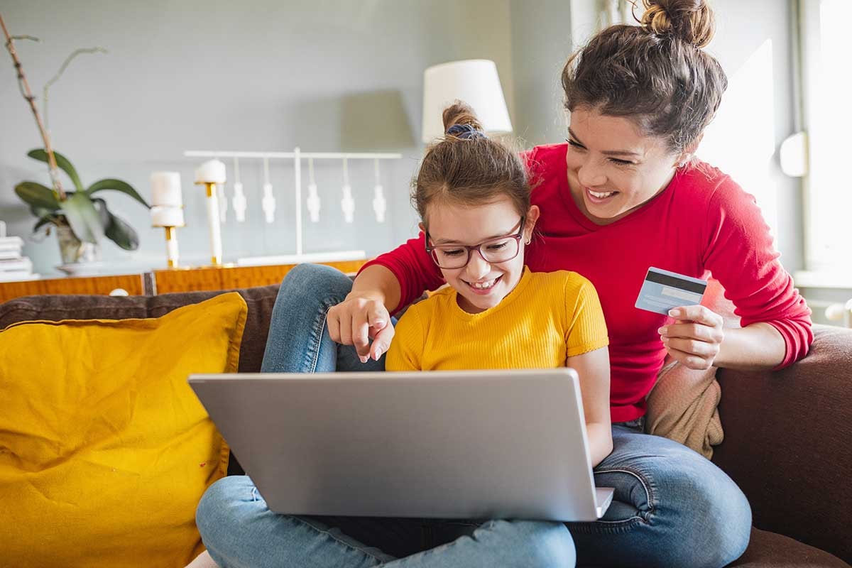 Mor og barn ser på pc med bankkort i handa, til illustrasjon og barn og penger