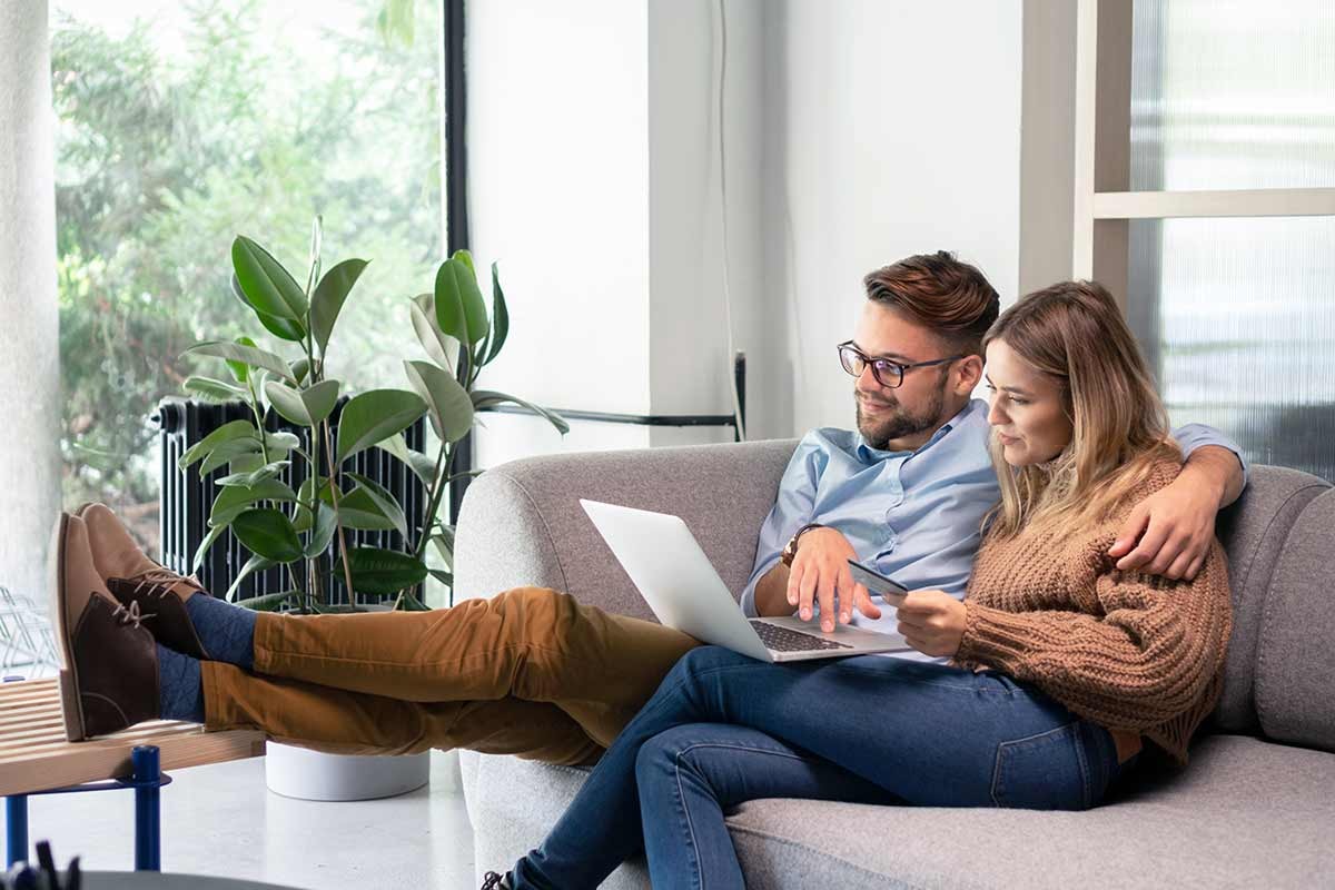 Par sitter i sofaen og ser på laptop, til illustrasjon for omkostninger ved boligkjøp