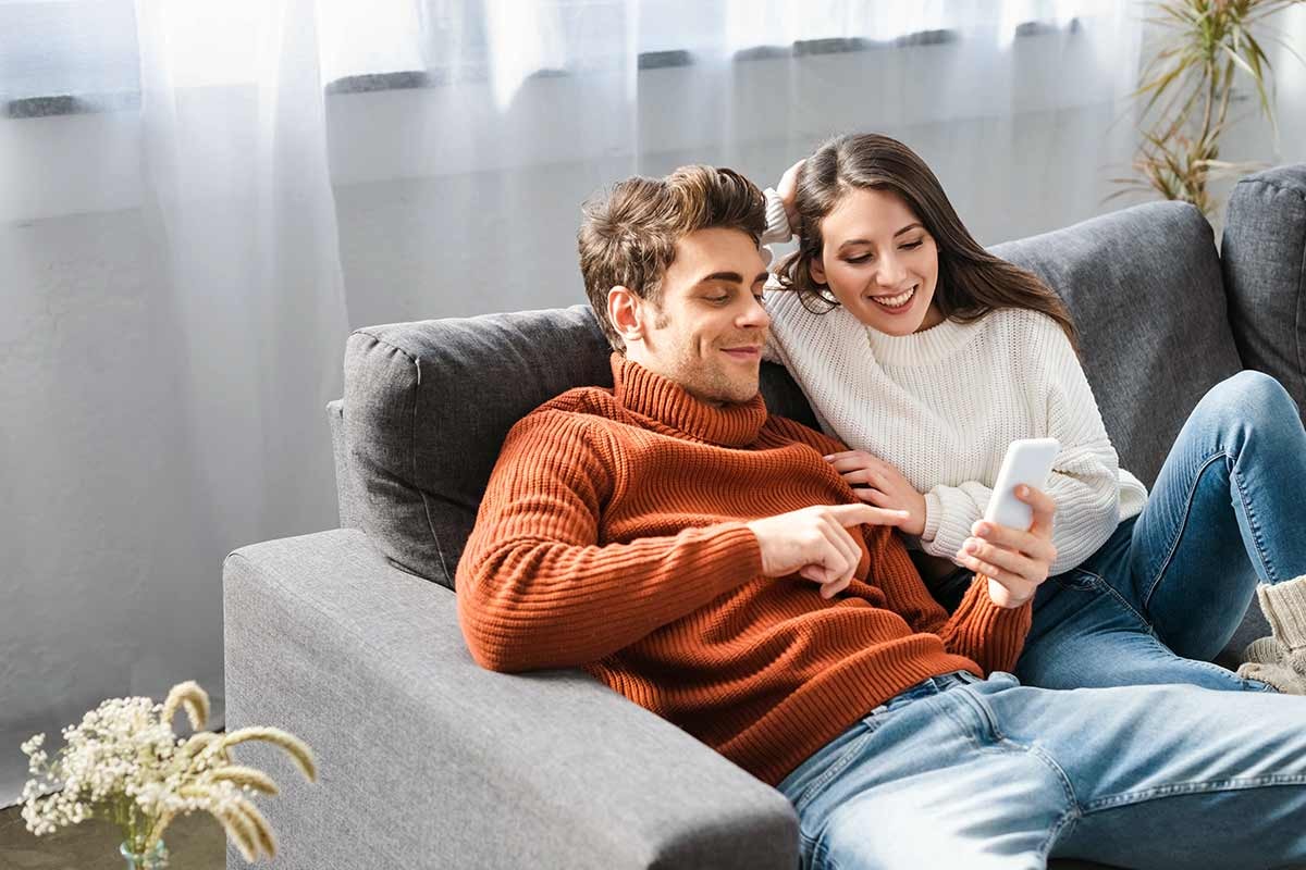 Par i sofa som ser på mobilen, til illustrasjon for få pengene til å vare lenger