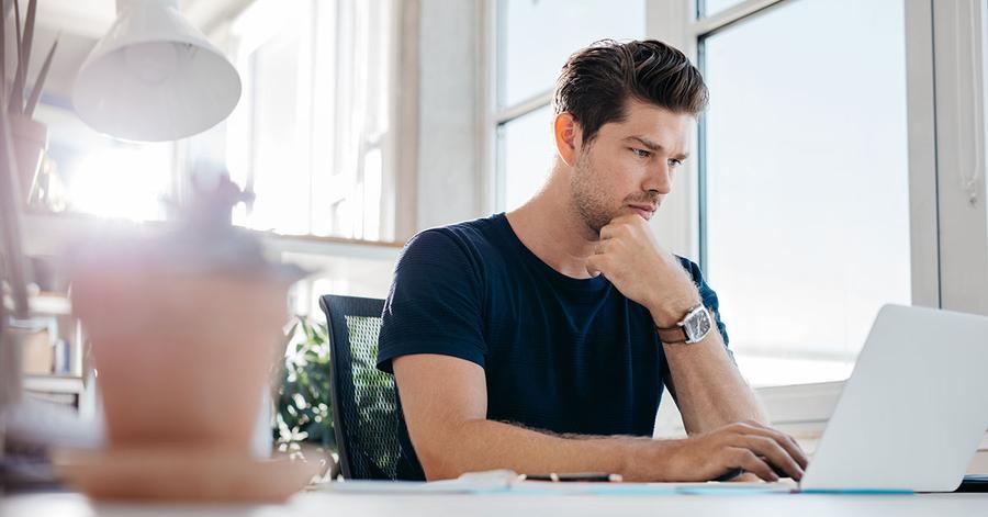 Ung mann sitter ved et skrivebord og leser på en pc, til illustrasjon for BSU-regler