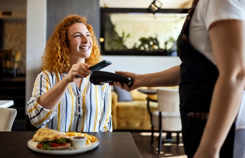 Dame betaler med mobiltelefonen på restaurant og smiler, til illustrasjon for Samsung Pay