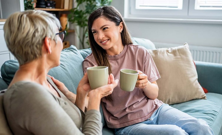 To kvinner sitter i en sofa og drikker kaffe, i forbindelse med hvordan hjelpe barna inn på boligmarkedet
