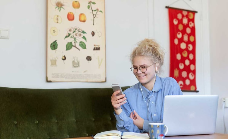 Jente sitter i grønn sofa og ser på mobilen med hodetelefoner, til illustrasjon for husleiekontrakt