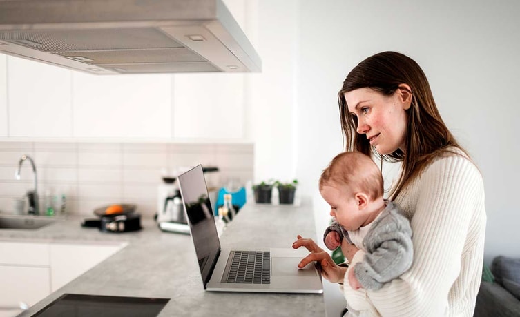 Mor med baby på fanget ved laptop, til illustrasjon for regningskonto