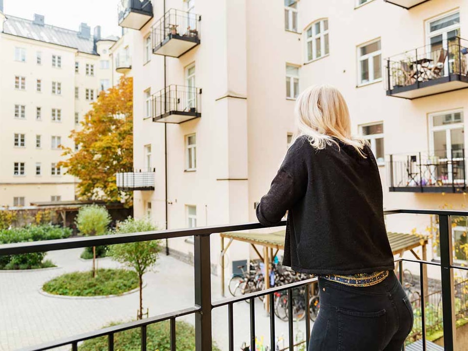 Dame på balkong ser utover bygård, til illustrasjon for selveier, andel og aksjeleilighet
