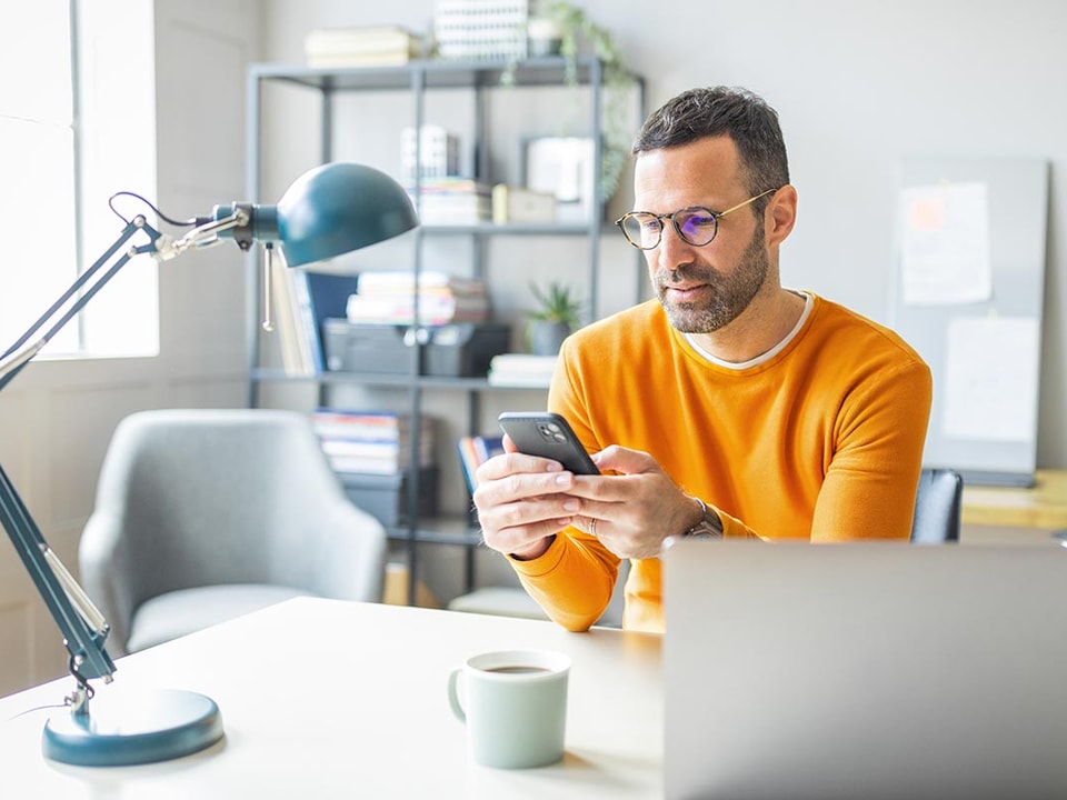 Mann i orange genser ser på mobilen, til illustrasjon for mine kort app