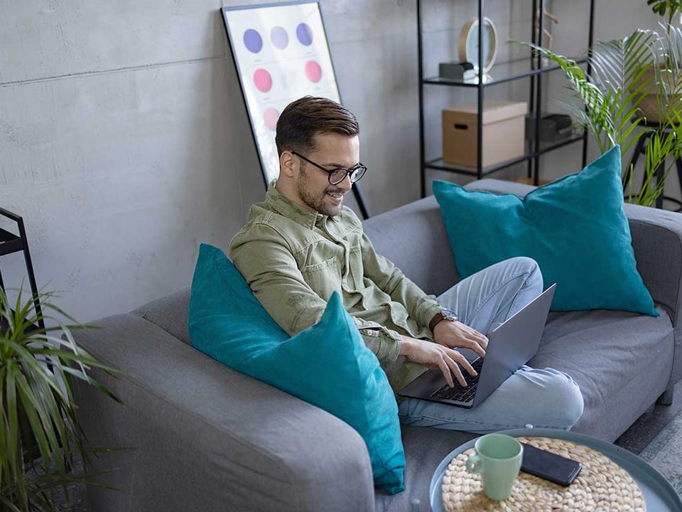Mann sitter i sofa og jobber på PC, til illustrasjon for hvordan spare penger