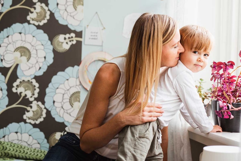 Mor gir sønn en klem mens han lener seg inn i vinduskarmen