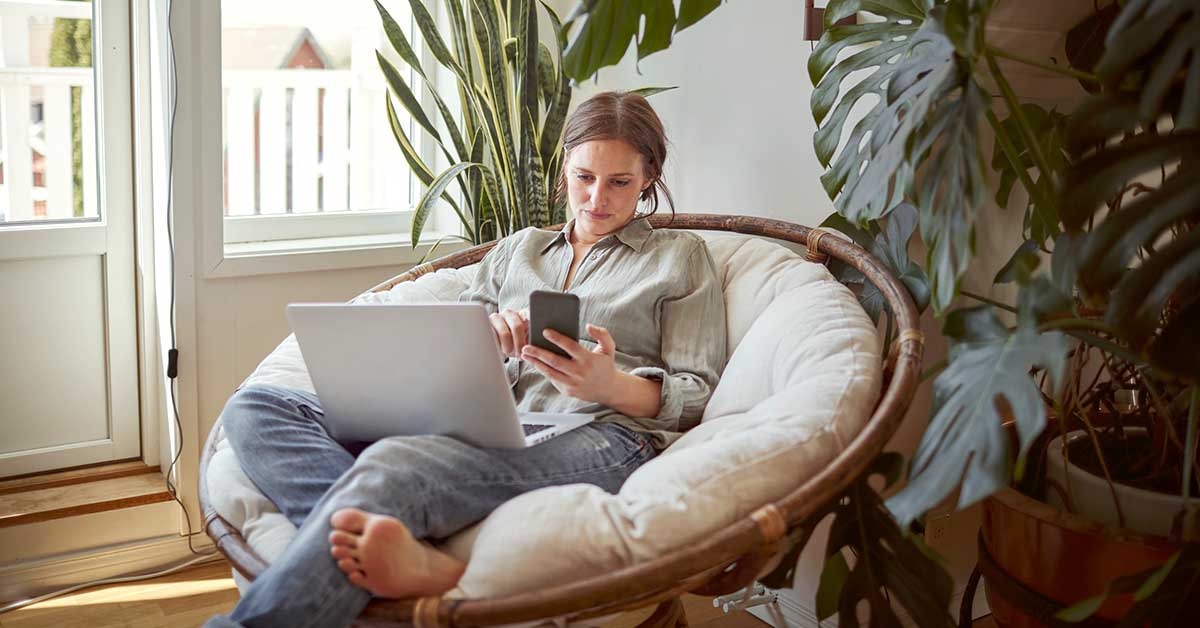 Dame slapper av i stolen med mobil og pc, til illustrasjon for økt boliglånsrente