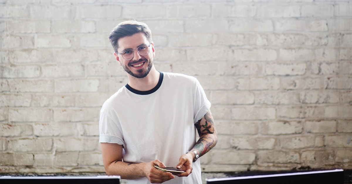 Ung mann fremfor murvegg holder en notatblokk, til illustrasjon for kjøpe første bolig