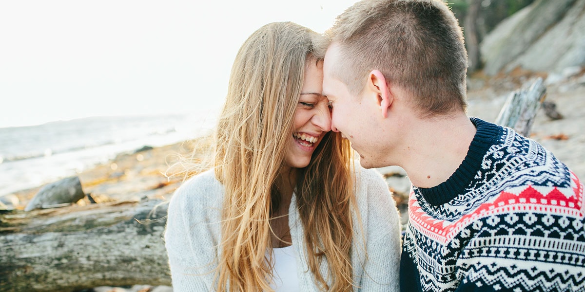 Par sitter på stranda og ler, til illustrasjon for å kjøpe seg inn i bolig