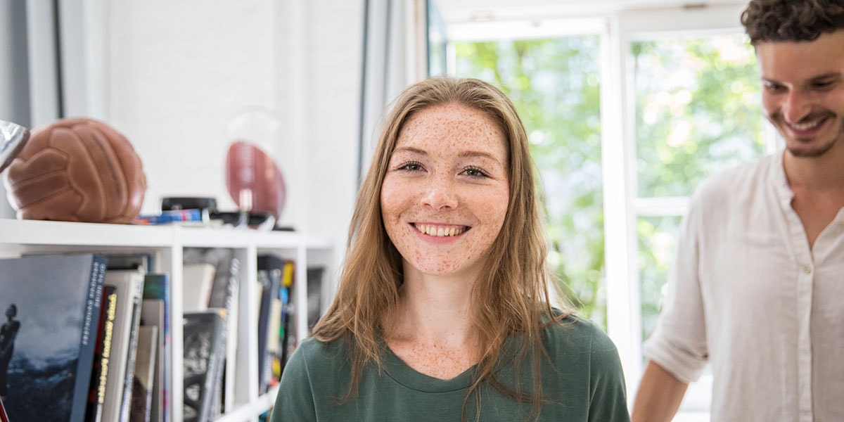 Jente står i leilighet og smiler mens en mann er bak henne, til illustrasjon for medlåntaker