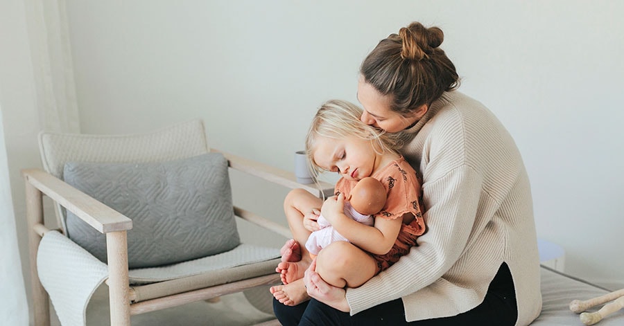 En mor sitter i stuen med datteren på fanget, til illustrasjon for et boligkjøp med pant i bolig