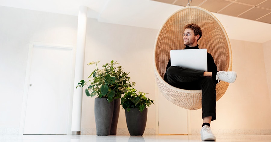 Mann sitter i hengestol med laptop og grønne planter ved siden, til illustrasjon for hva følger med boligen ved salg