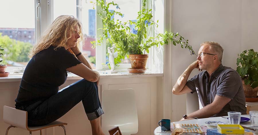 En kvinne og en mann sitter ved et vindu og prater med alvor, til illustrasjon for samlivsbrudd og økonomi