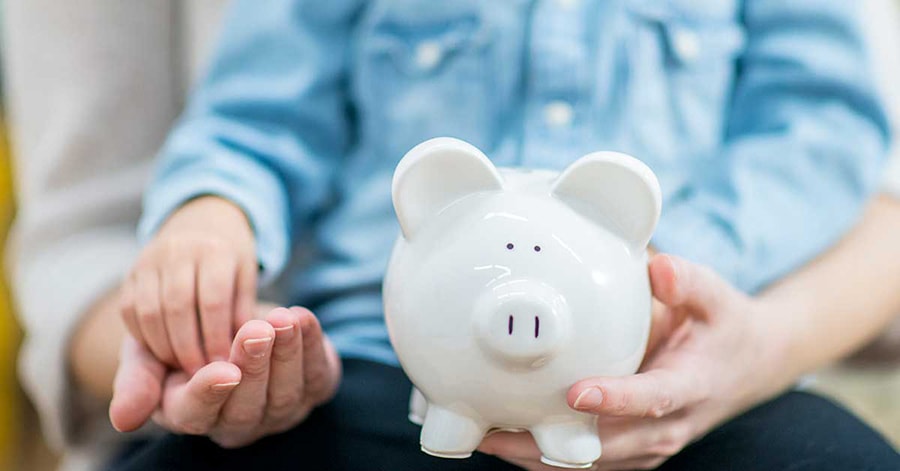 Barn sitter i fanget til mor og holder en sparegris, til illustrasjon for spare til barna