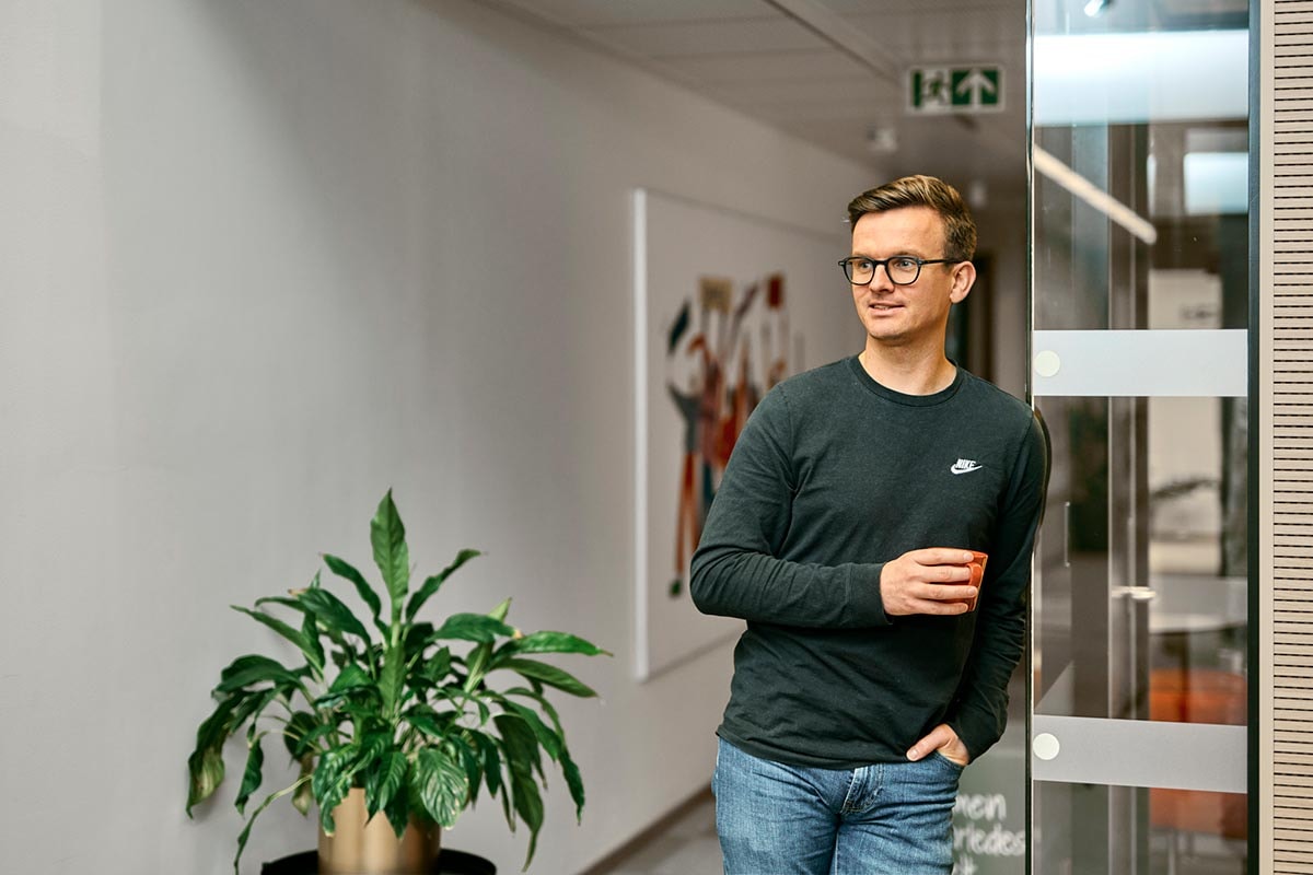 BN Bank ansatt Mathias lener seg mot glassvegg og holder en kaffekopp, til illustrasjon for AS eller ENK