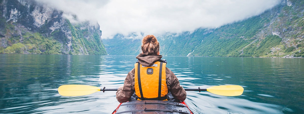 Kvinne er ute på kajakktur og ser ut over landskapet, til illustrasjon for Norgesferie