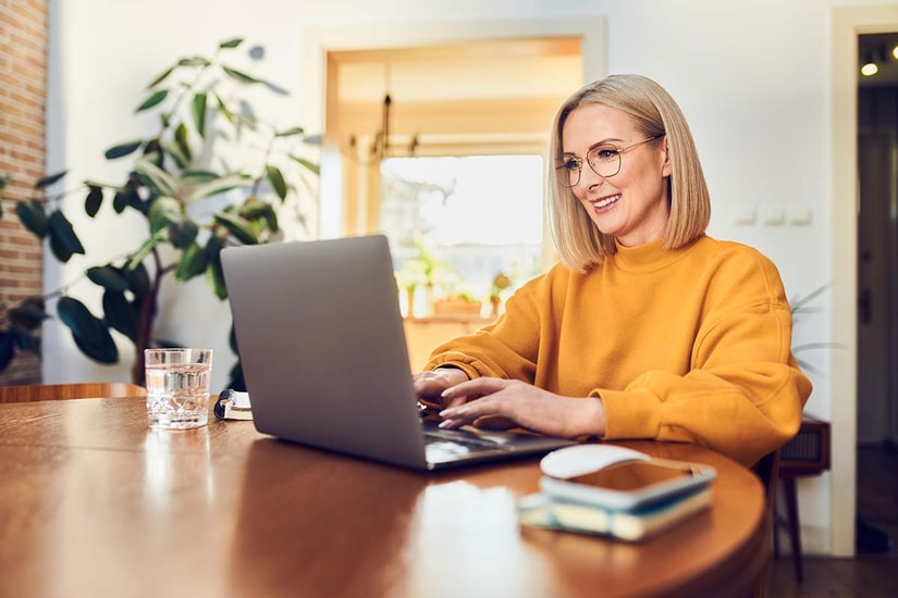 Dame i oransje grenser sitter ved spisebord og ser på datamaskin, til illustrasjon for betale til utlandet