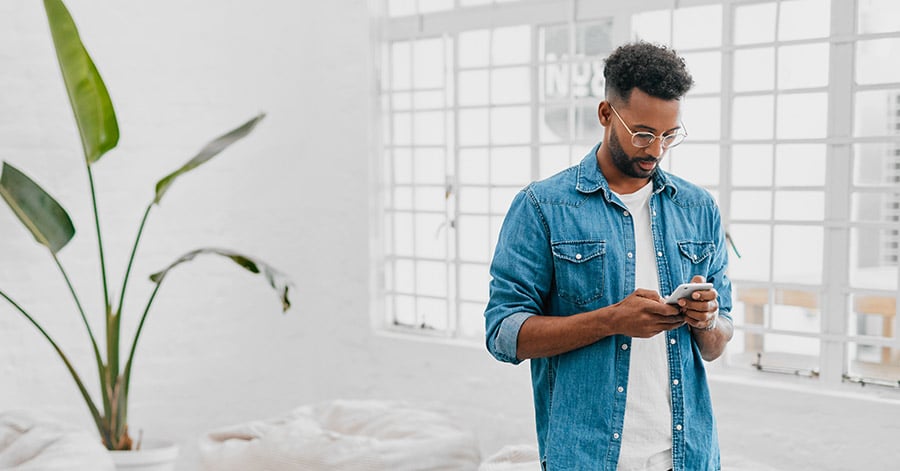 Ung mann i denim skjorte ser på mobilen, til illustrasjon for mine kort app