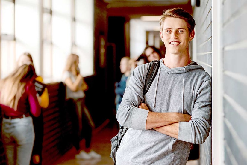 Gutt i grå hettegenser lener seg mot vegg og smiler, til illustrasjon for BSU-konto