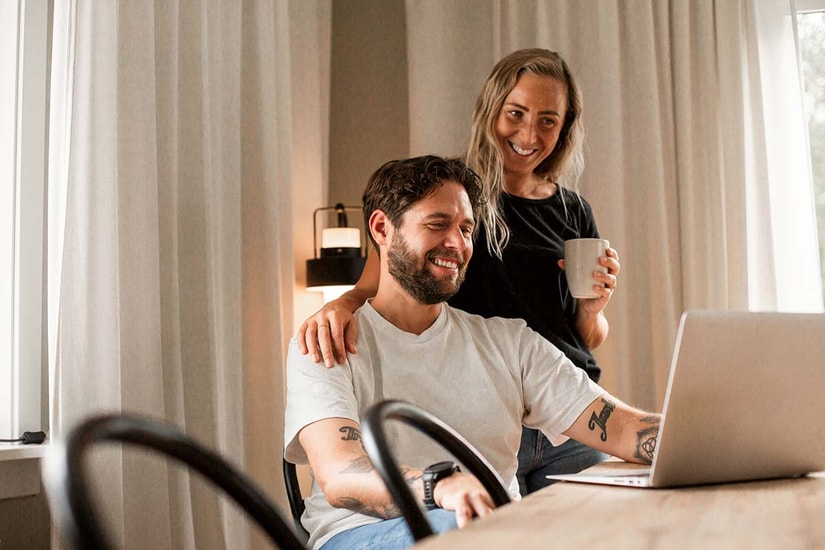 Kvinne holder armen sin rundt en mann som sitter og jobber på PC, til illustrasjon for høyrentekonto