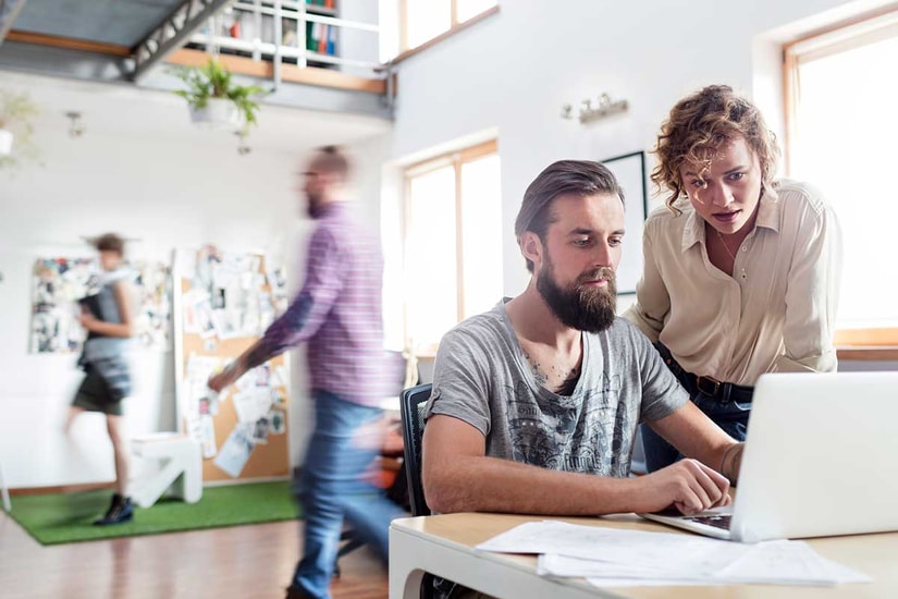 Åpent kontorlandskap med en mann og en dame som ser på en PC, til illustrasjon for betalingstjenester