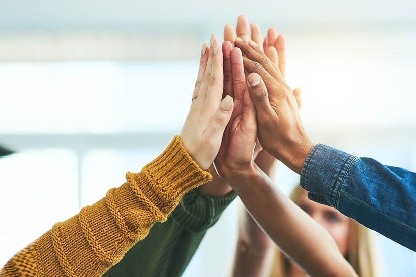 En gruppe menesker hever hendene i været, som symbol på samarbeid og vennskap