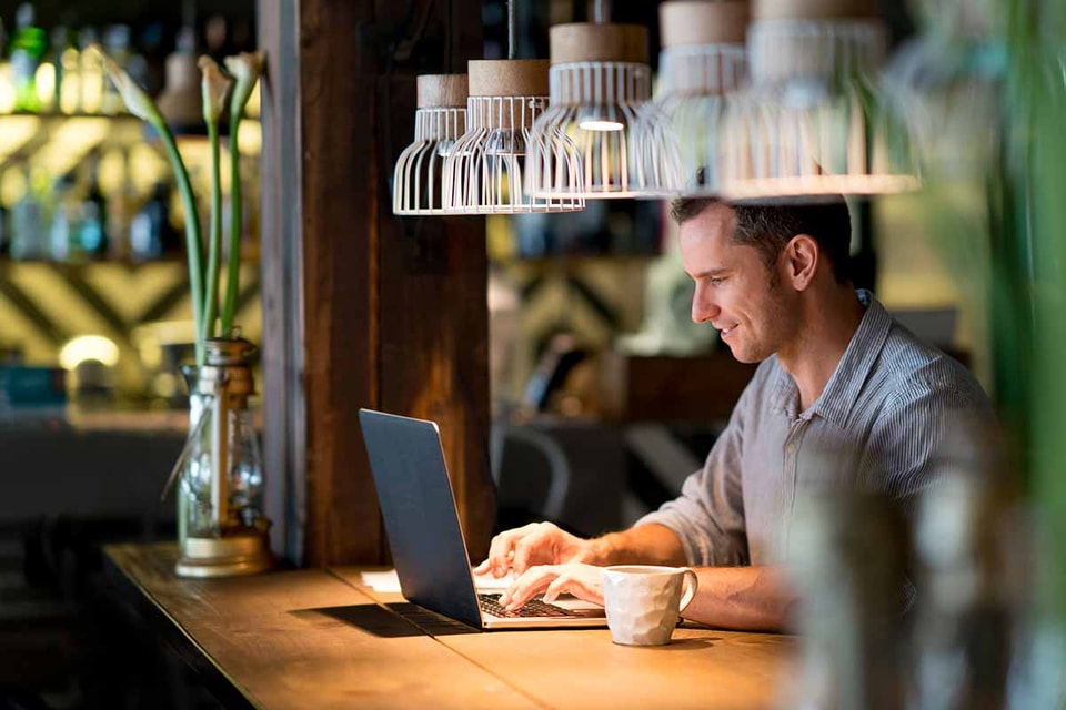 Mann sitter på cafe og ser på laptop, til illustrasjon for mobil-og nettbank