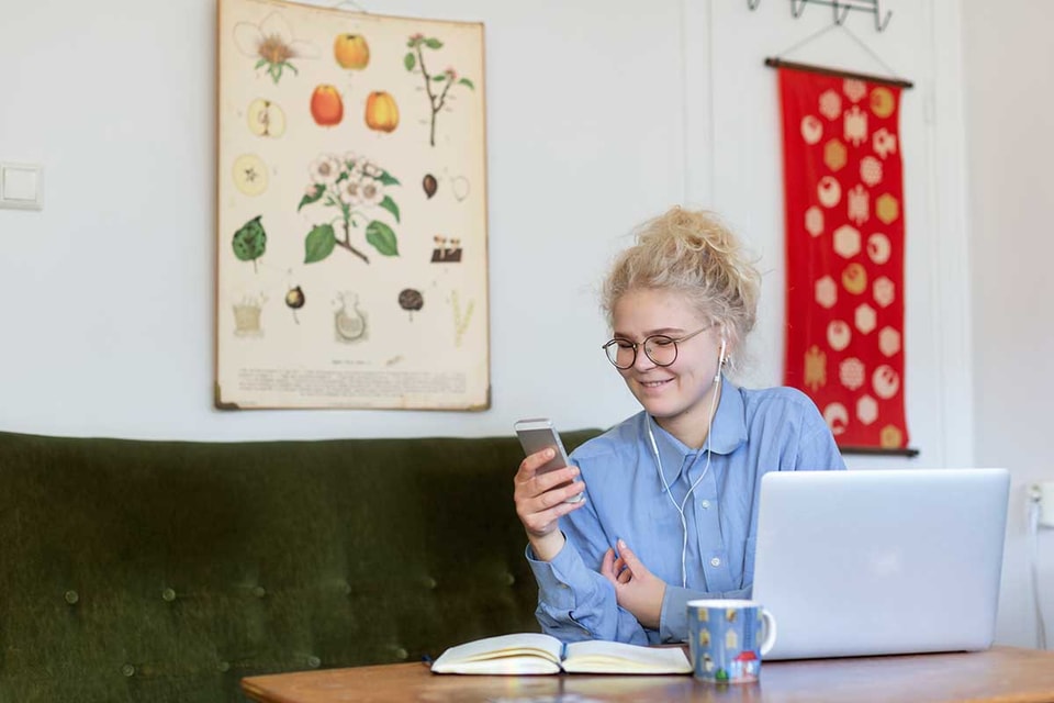 Jente sitter i grønn sofa og ser på mobilen med hodetelefoner, til illustrasjon for husleiekontrakt