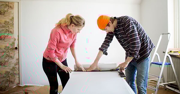 Dame og mann måler tapet mens de pusser opp, til illustrasjon for låne eller spare til oppussing