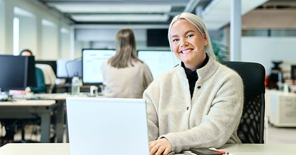 Boliglånsrådgiver i BN Bank, Emilie, sitter i lokalet fremfor en PC og smiler, til illustrasjon for rentekalkulator