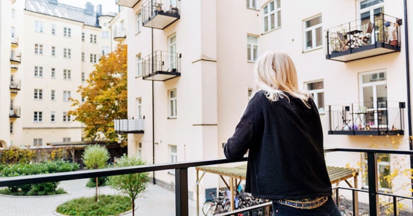 Dame på balkongen ser utover bygård, til illustrasjon for selveier, andel og aksjeleiliighet