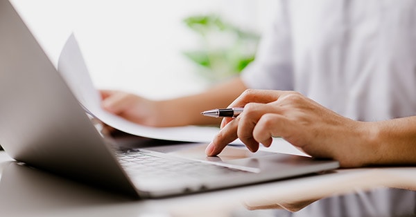 Person fyller ut skjema, holder en penn og ser på PC, til illustrasjon for tips før visning