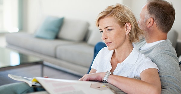 Dame sitter i sofa med et magasin og lener seg på en mann, til illustrasjon for salg av bolig