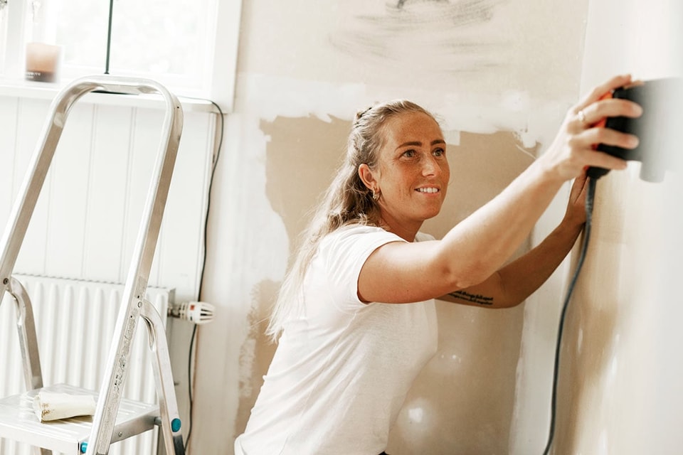 Dame sitter på gulvet og sliper veggen, til illustrasjon for hvor mye koster det å pusse opp leilighet