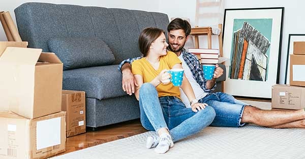 Par sitter i stua med flytteesker og bilder rundt seg, til illustrasjon for bolig