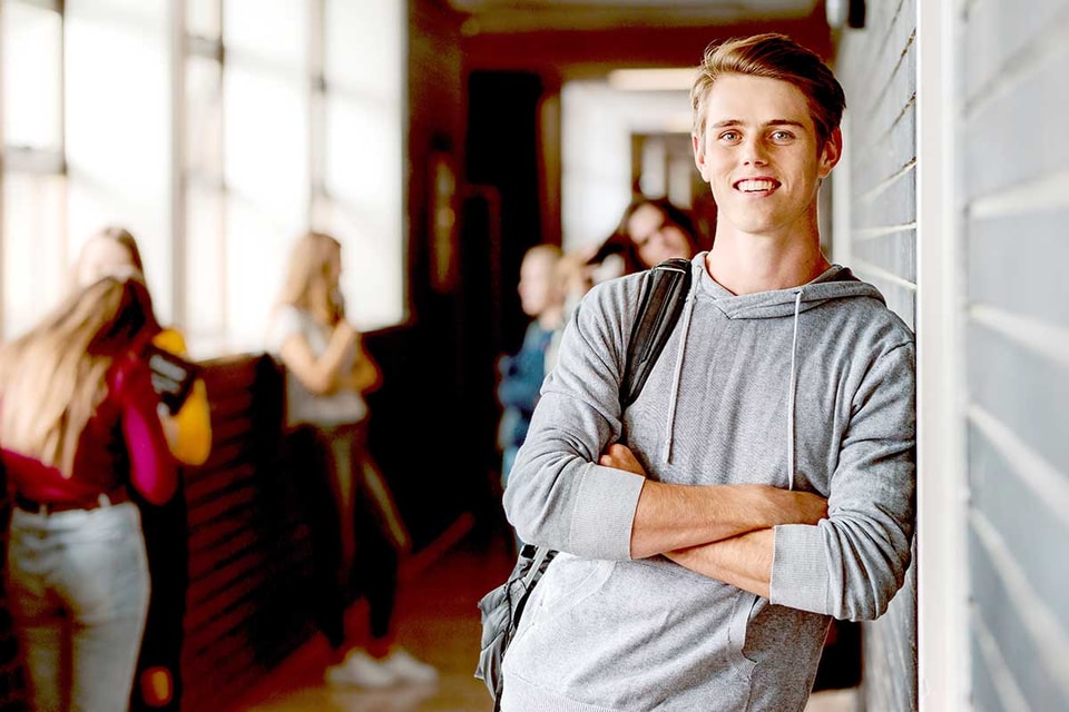 Gutt i grå hettegenser lener seg mot vegg og smiler, til illustrasjon for BSU-konto