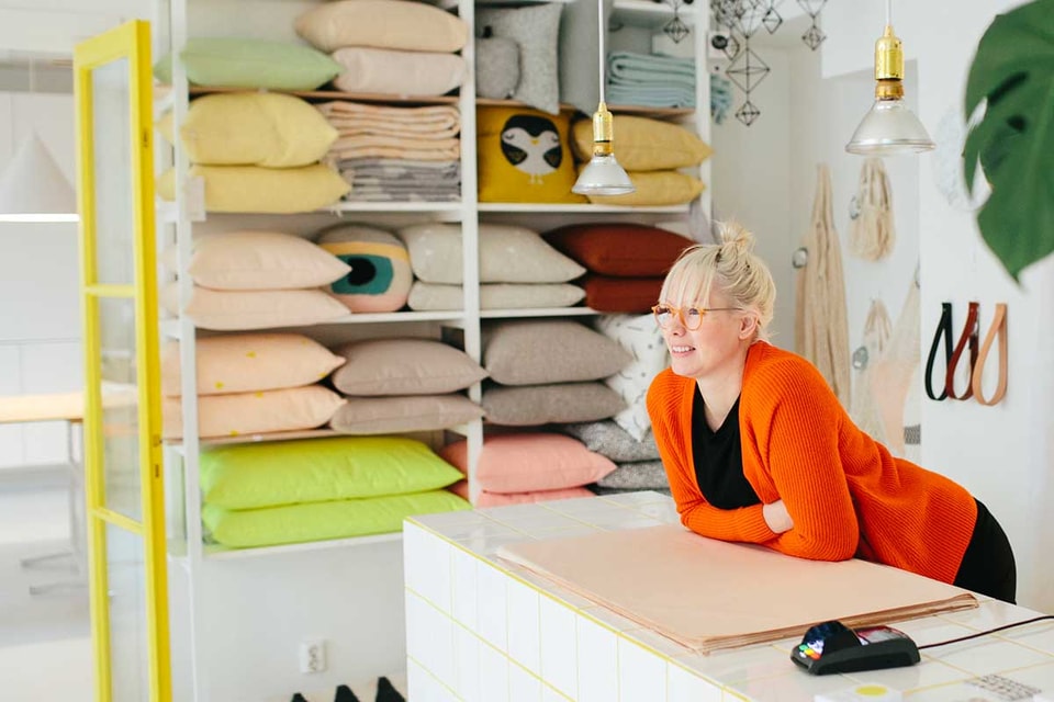 Dame lener seg over disken i interiørbutikken sin med betalingsterminal rett ved