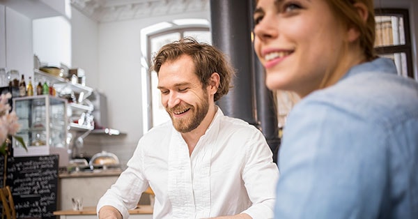 Mann og dame smiler på kafé, til illustrasjon for starte AS