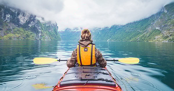 Jente ute på padletur i kajakk og ser ut over landskapet mens hun er på Norgesferie