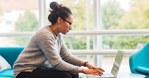 Kvinne sitter i en blå sofa og jobber på PC, til illustrasjon for å unngå skattesmell