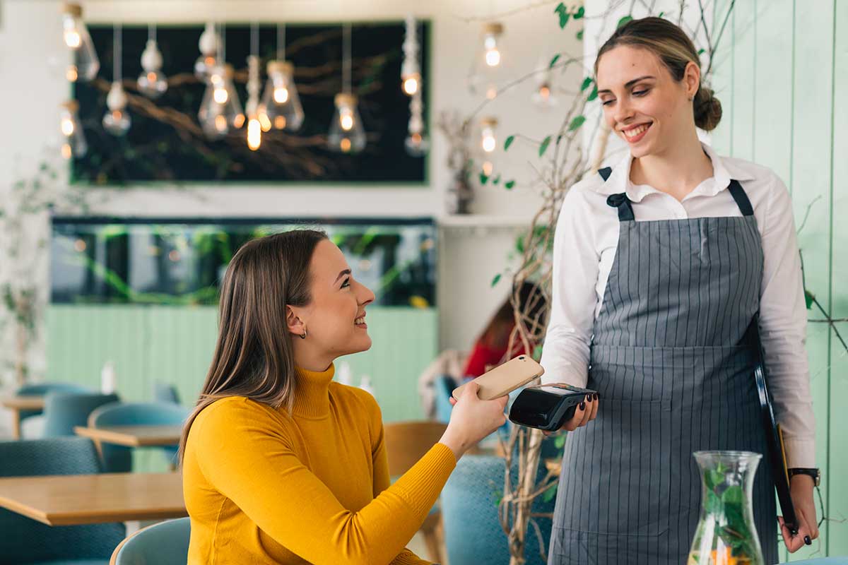 Dame sitter på kafé og betaler med mobiltelefonen til servitør