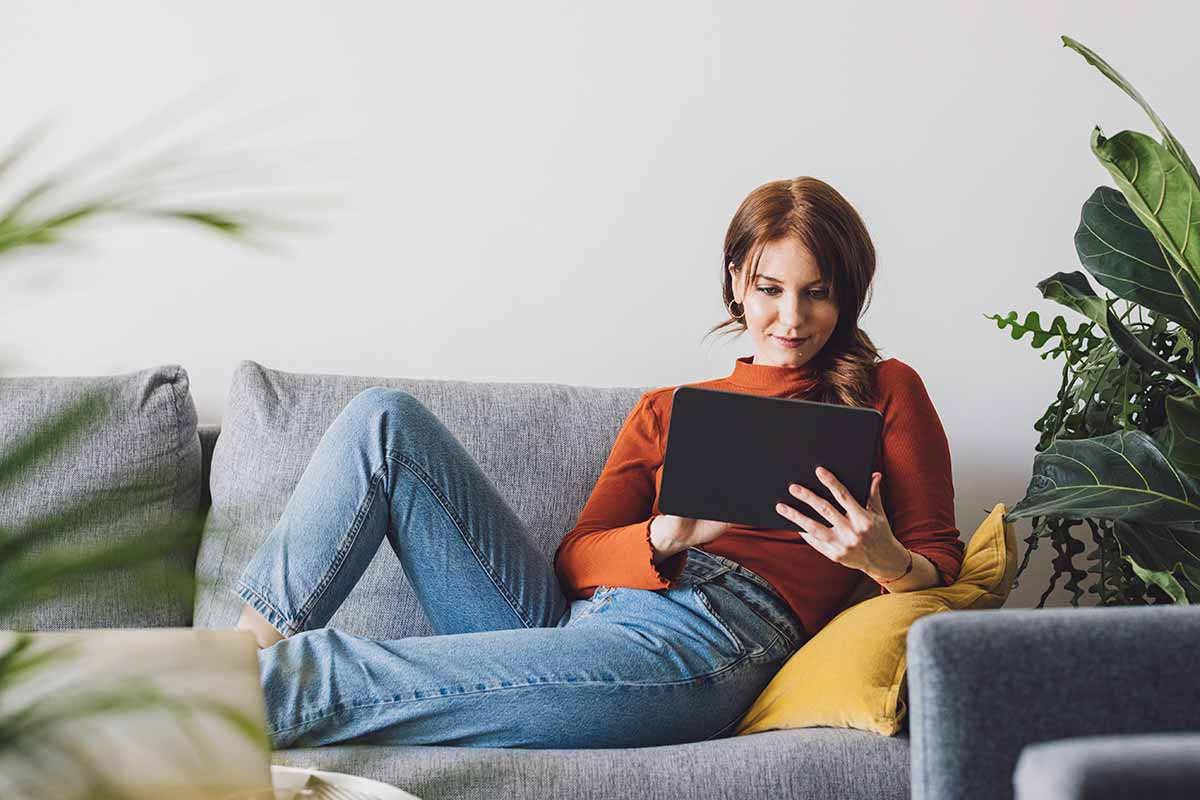 Dame sitter i sofa og leser på nettbrett, til illustrasjon for logg inn i bn bank