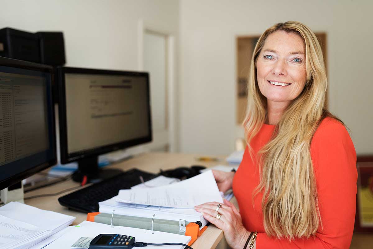 Kvinne sitter ved en pult med en stor bok med dokumenter for å få kontroll på økonomien