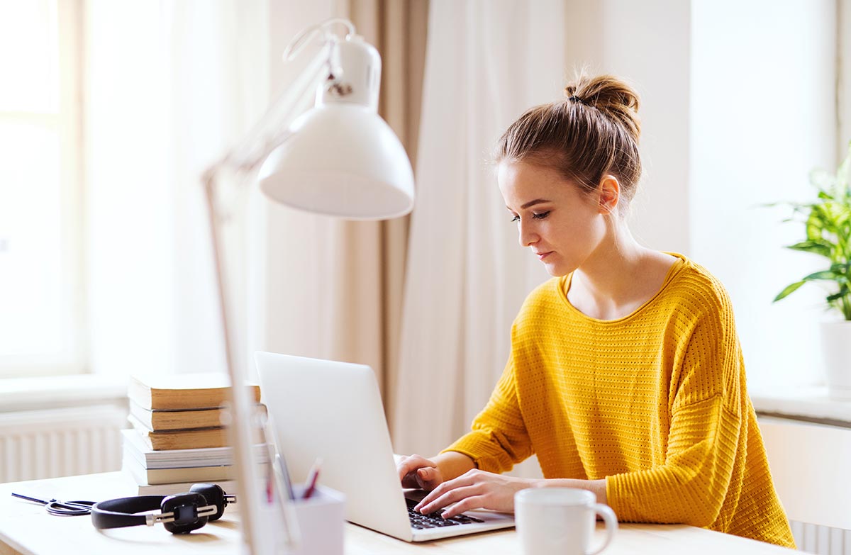 Jente i orange genser med PC, til illustrasjon for ung voksen på vei inn i voksenlivet