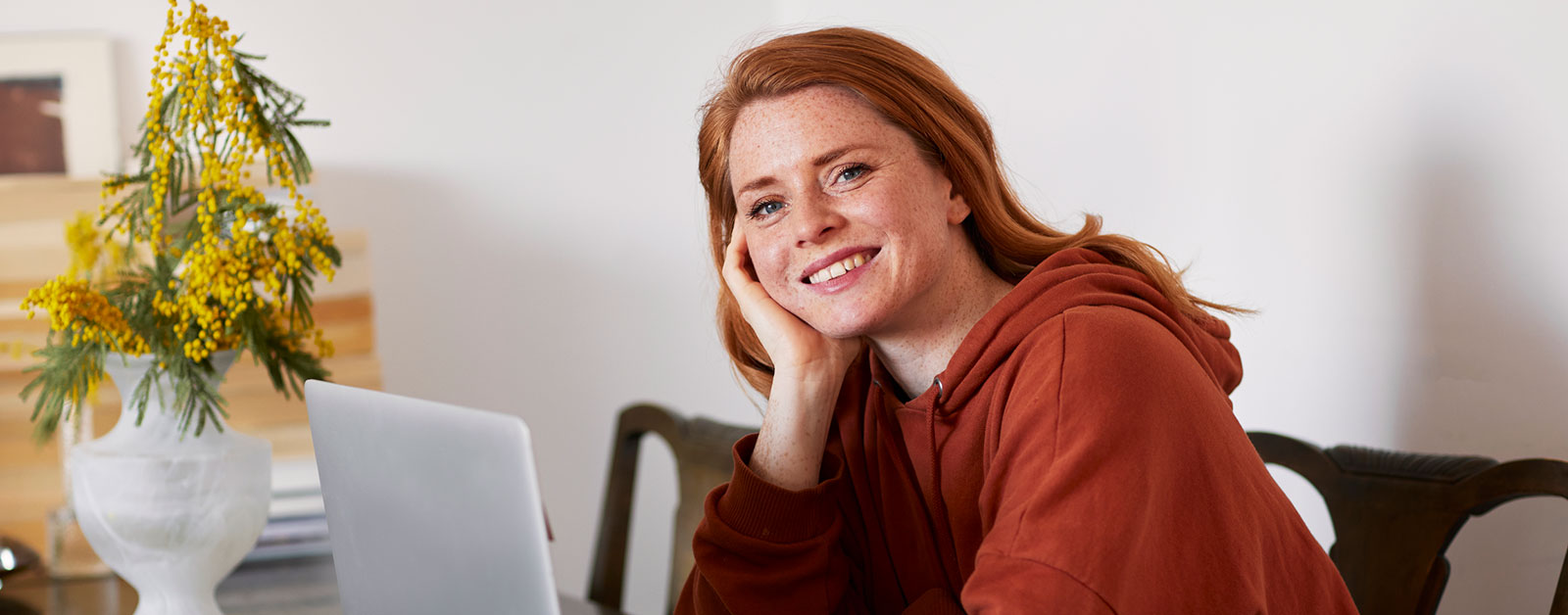 Ung jente sitter på kjøkkenbord med datamaskin fremfor seg og smiler, til illustrasjon for sparekalkulator